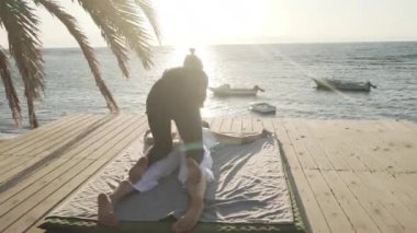 Güneş doğarken ahşap bir zeminde Tayland yogası yapan yakışıklı genç bayan.