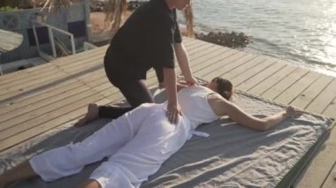 Güneş doğarken ahşap bir zeminde Tayland yogası yapan yakışıklı genç bayan.