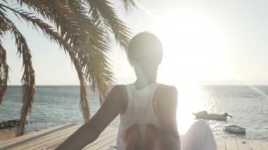 Genç bir kadın güneş doğarken ahşap bir zeminde Tayland yogası yapıyor.