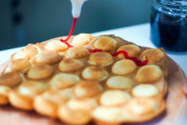 Aşçı, Hong Kong waffle 'larını dondurma, reçel ve meyve ile hazırlar. Hong Kong balonlu gofret tutan genç bir kadın.