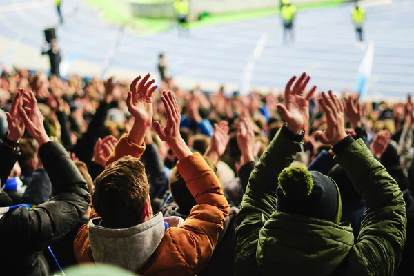 Football fans raising hands, chanting, supporting national team at stadium