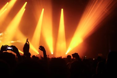 Konserin siluetleri parlak sahne ışıkları önünde kalabalık. Gece hayatı ve konser parti konsept.