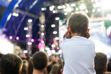 Çocuk bir açık hava rock müzik konserinde onlarla el ele tutuşarak ailesinin omuzlarında eğlenceli