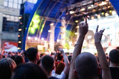 Konser kalabalık bir konser, insan siluetleri katılıyor mu görünür, arkadan aydınlatmalı sahne ışıkları tarafından. Yükseltilmiş elleri ve akıllı telefonlar orada burada görülebilir.