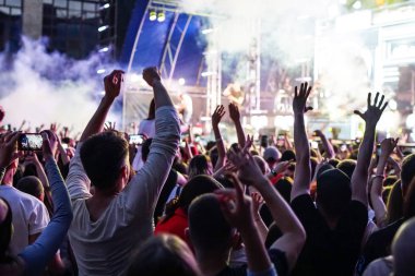 Konser kalabalık bir konser, insan siluetleri katılıyor mu görünür, arkadan aydınlatmalı sahne ışıkları tarafından. Yükseltilmiş elleri ve akıllı telefonlar orada burada görülebilir.