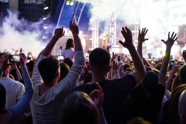 Konser kalabalık bir konser, insan siluetleri katılıyor mu görünür, arkadan aydınlatmalı sahne ışıkları tarafından. Yükseltilmiş elleri ve akıllı telefonlar orada burada görülebilir.