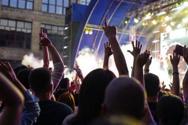 Konser kalabalık bir konser, insan siluetleri katılıyor mu görünür, arkadan aydınlatmalı sahne ışıkları tarafından. Yükseltilmiş elleri ve akıllı telefonlar orada burada görülebilir.