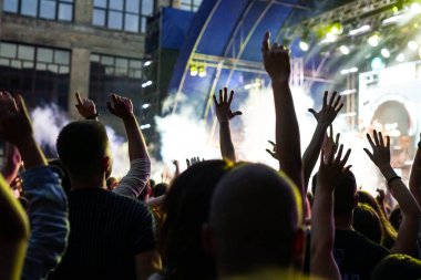 Konser kalabalık bir konser, insan siluetleri katılıyor mu görünür, arkadan aydınlatmalı sahne ışıkları tarafından. Yükseltilmiş elleri ve akıllı telefonlar orada burada görülebilir.