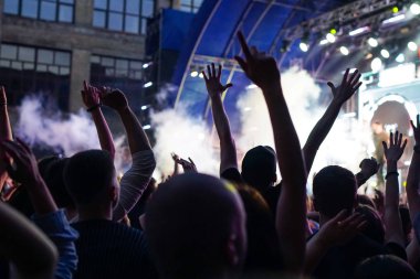 Konser kalabalık bir konser, insan siluetleri katılıyor mu görünür, arkadan aydınlatmalı sahne ışıkları tarafından. Yükseltilmiş elleri ve akıllı telefonlar orada burada görülebilir.