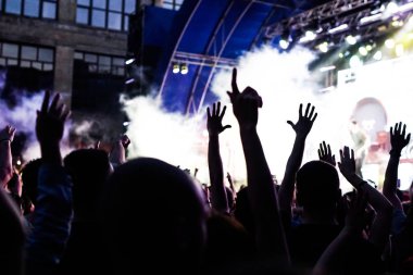 Konser kalabalık bir konser, insan siluetleri katılıyor mu görünür, arkadan aydınlatmalı sahne ışıkları tarafından. Yükseltilmiş elleri ve akıllı telefonlar orada burada görülebilir.