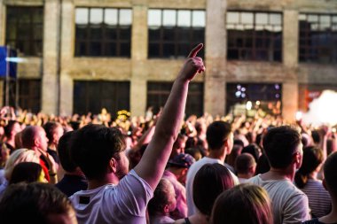 Konser kalabalık bir konser, insan siluetleri katılıyor mu görünür, arkadan aydınlatmalı sahne ışıkları tarafından. Yükseltilmiş elleri ve akıllı telefonlar orada burada görülebilir.