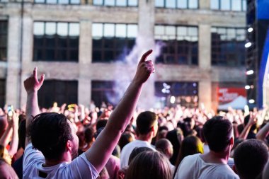 Konser kalabalık bir konser, insan siluetleri katılıyor mu görünür, arkadan aydınlatmalı sahne ışıkları tarafından. Yükseltilmiş elleri ve akıllı telefonlar orada burada görülebilir.