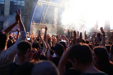 Konser kalabalık bir konser, insan siluetleri katılıyor mu görünür, arkadan aydınlatmalı sahne ışıkları tarafından. Yükseltilmiş elleri ve akıllı telefonlar orada burada görülebilir.