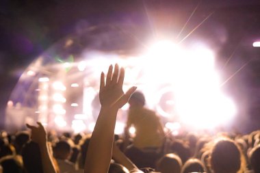 Konser kalabalık bir konser, insan siluetleri katılıyor mu görünür, arkadan aydınlatmalı sahne ışıkları tarafından. Yükseltilmiş elleri ve akıllı telefonlar orada burada görülebilir.