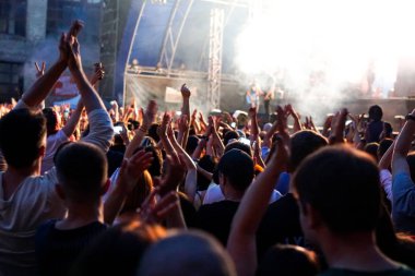 Konser kalabalık bir konser, insan siluetleri katılıyor mu görünür, arkadan aydınlatmalı sahne ışıkları tarafından. Yükseltilmiş elleri ve akıllı telefonlar orada burada görülebilir.