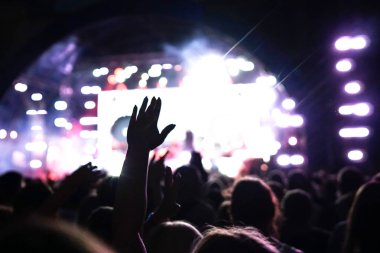 Konser kalabalık bir konser, insan siluetleri katılıyor mu görünür, arkadan aydınlatmalı sahne ışıkları tarafından. Yükseltilmiş elleri ve akıllı telefonlar orada burada görülebilir.