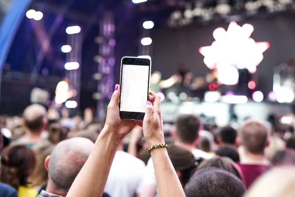 Konser kalabalık bir konser, insan siluetleri katılıyor mu görünür, arkadan aydınlatmalı sahne ışıkları tarafından. Yükseltilmiş elleri ve akıllı telefonlar orada burada görülebilir.