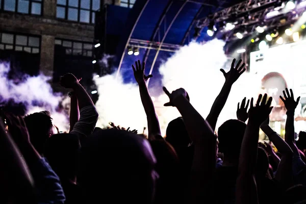 La folla di concerto che assiste a un concerto, le sagome della gente sono visibili, retroilluminate da luci di scena. Mani alzate e smartphone sono visibili qua e là . — Foto Stock
