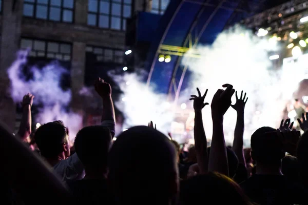 Multitud de conciertos asistiendo a un concierto, las siluetas de la gente son visibles, retroiluminadas por luces de escenario. Las manos levantadas y los teléfonos inteligentes son visibles aquí y allá . — Foto de Stock