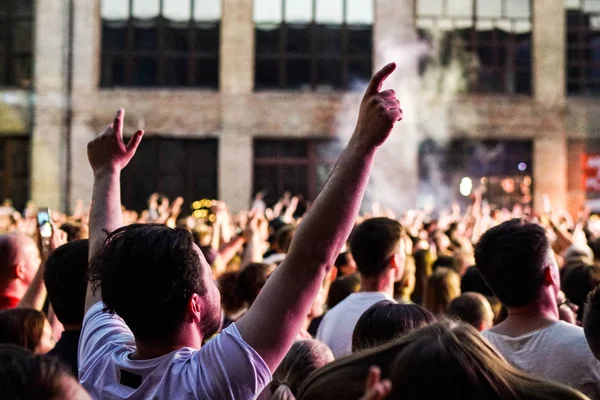 Konser kalabalık bir konser, insan siluetleri katılıyor mu görünür, arkadan aydınlatmalı sahne ışıkları tarafından. Yükseltilmiş elleri ve akıllı telefonlar orada burada görülebilir.