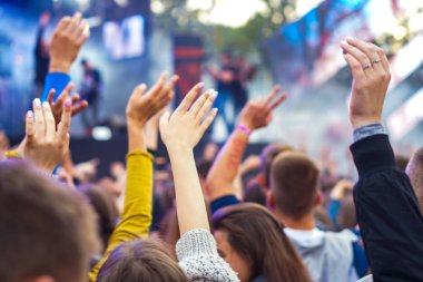 Bir müzik festivalinde seyirciler ellerini kaldırdı ve sahnenin üstünden ışıklar süzülüyor..