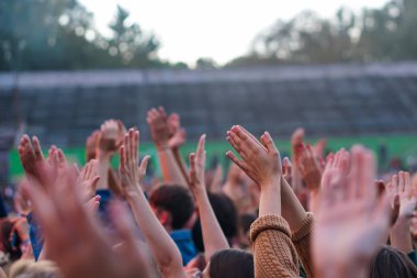 Bir müzik festivalinde seyirciler ellerini kaldırdı ve sahnenin üstünden ışıklar süzülüyor..