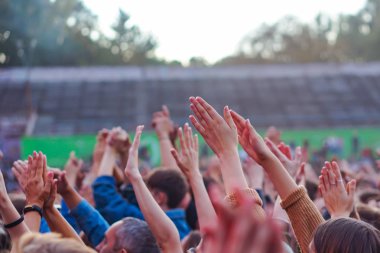 Bir müzik festivalinde seyirciler ellerini kaldırdı ve sahnenin üstünden ışıklar süzülüyor..
