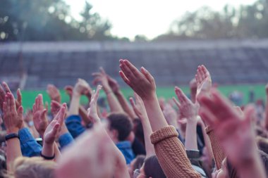 Bir müzik festivalinde seyirciler ellerini kaldırdı ve sahnenin üstünden ışıklar süzülüyor..