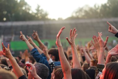 Bir müzik festivalinde seyirciler ellerini kaldırdı ve sahnenin üstünden ışıklar süzülüyor..