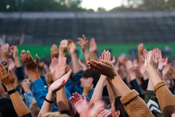 Audience with hands raised at a music festival and lights streaming down from above the stage. — Stock Photo, Image