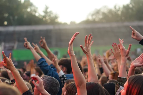Publiken med händerna upphöjda på en musikfestival och ljus strömmande ner från ovan scenen. — Stockfoto
