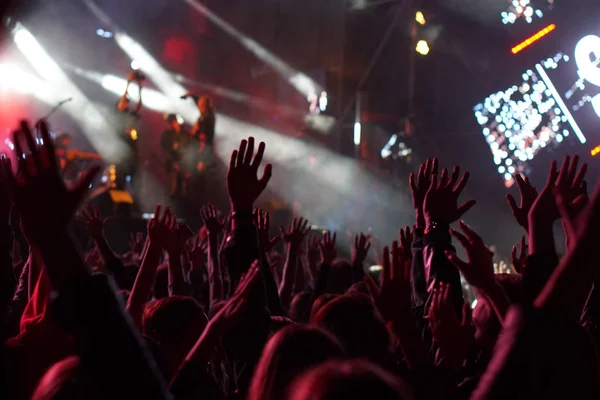 Audience with hands raised at a music festival and lights streaming down from above the stage. — Stock Photo, Image