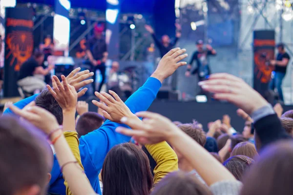 Audience with hands raised at a music festival and lights streaming down from above the stage. — Stock Photo, Image