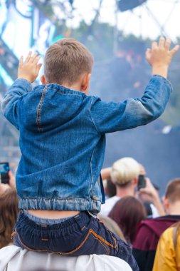 Çocuk bir açık hava rock müzik konserinde onlarla el ele tutuşarak ailesinin omuzlarında eğlenceli