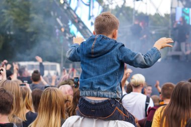 Çocuk bir açık hava rock müzik konserinde onlarla el ele tutuşarak ailesinin omuzlarında eğlenceli
