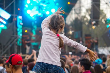 Çocuk bir açık hava rock müzik konserinde onlarla el ele tutuşarak ailesinin omuzlarında eğlenceli