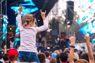 Çocuk bir açık hava rock müzik konserinde onlarla el ele tutuşarak ailesinin omuzlarında eğlenceli