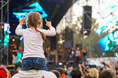 Çocuk bir açık hava rock müzik konserinde onlarla el ele tutuşarak ailesinin omuzlarında eğlenceli