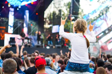 Çocuk bir açık hava rock müzik konserinde onlarla el ele tutuşarak ailesinin omuzlarında eğlenceli