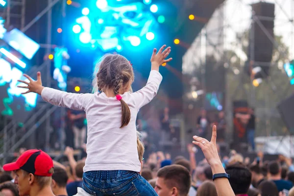 Çocuk bir açık hava rock müzik konserinde onlarla el ele tutuşarak ailesinin omuzlarında eğlenceli