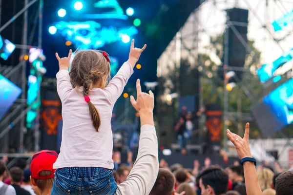 子供は、屋外のロックミュージックコンサートで彼らと手をつないで彼女の両親の肩に楽しみを持っています — ストック写真