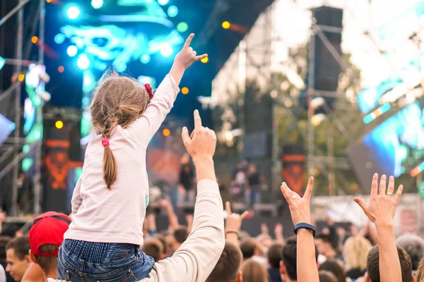 Çocuk bir açık hava rock müzik konserinde onlarla el ele tutuşarak ailesinin omuzlarında eğlenceli