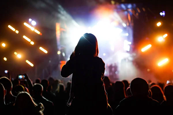 Criança se diverte nos ombros de seus pais mantendo as mãos com eles em um concerto de música rock ao ar livre — Fotografia de Stock