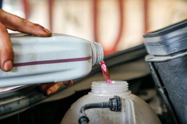 Caddedeki ön cam su tankına antifriz döken tamircinin yan görüntüsü