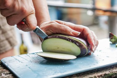 Kız sokakta ve yaz mutfağında patlıcan kesiyor.