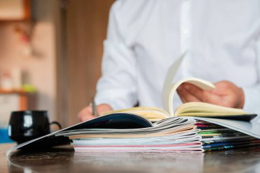 Yönetici bir günlüğe yazıyor, ön planda dergiler var.