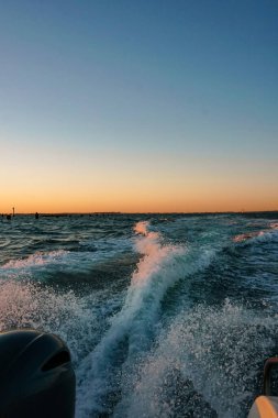 Güney sahilindeki kumsalda pembe turuncu gün batımı ve renkli mavi sörf dalgası kapanıyor.