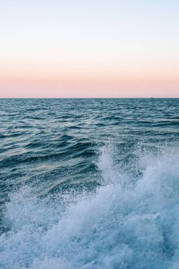 Güney sahilindeki kumsalda pembe turuncu gün batımı ve renkli mavi sörf dalgası kapanıyor.