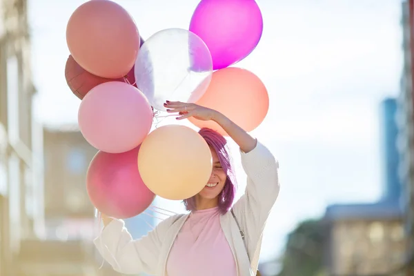 Frau mit lila Haaren steht mit Luftballons auf der Straße der Stadt Stockbild