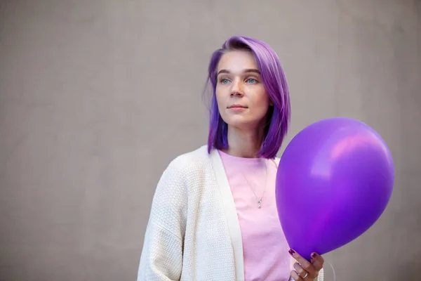 Woman with violet hair hold balloon in front of gray wall background